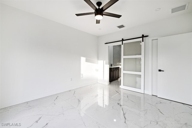 unfurnished bedroom featuring a barn door, ensuite bathroom, and ceiling fan