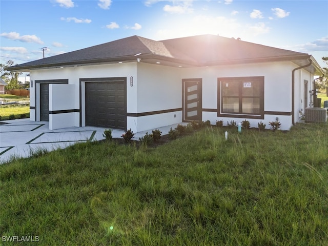 rear view of house featuring a garage, a lawn, and central AC unit