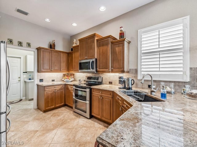 kitchen with sink, decorative backsplash, light tile patterned floors, light stone counters, and stainless steel appliances