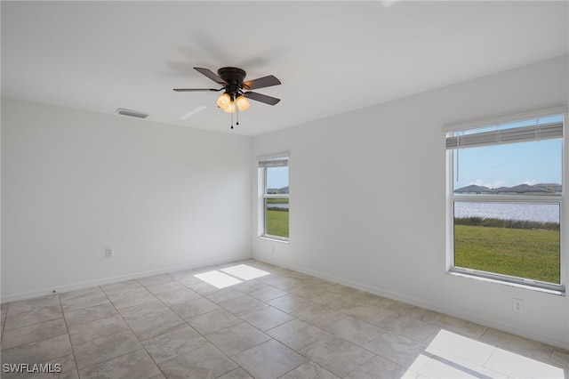 empty room with a water view, ceiling fan, and light tile patterned floors