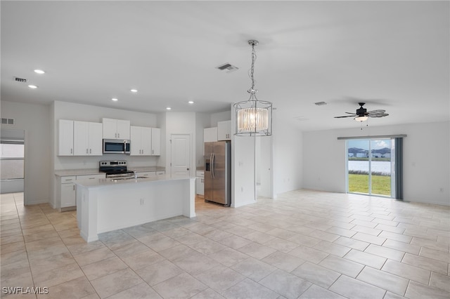 kitchen with a kitchen island with sink, hanging light fixtures, white cabinets, appliances with stainless steel finishes, and ceiling fan with notable chandelier