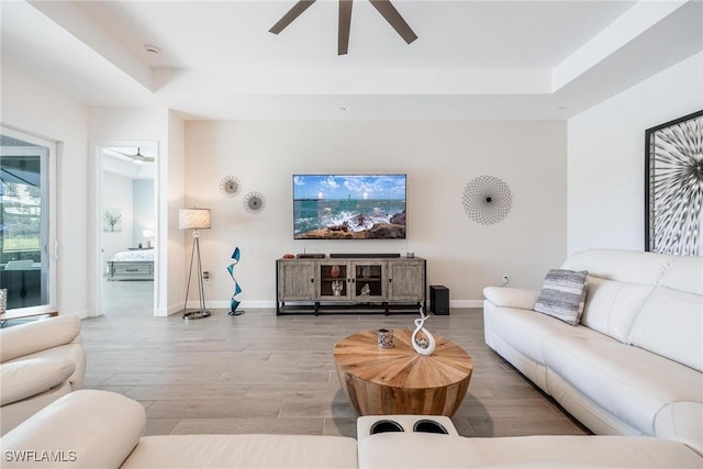 living area with a tray ceiling, wood finished floors, a ceiling fan, and baseboards