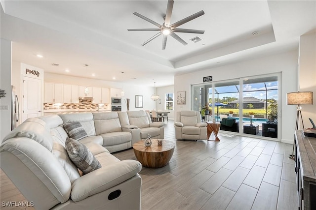 living room with ceiling fan, visible vents, a raised ceiling, and light wood-style flooring