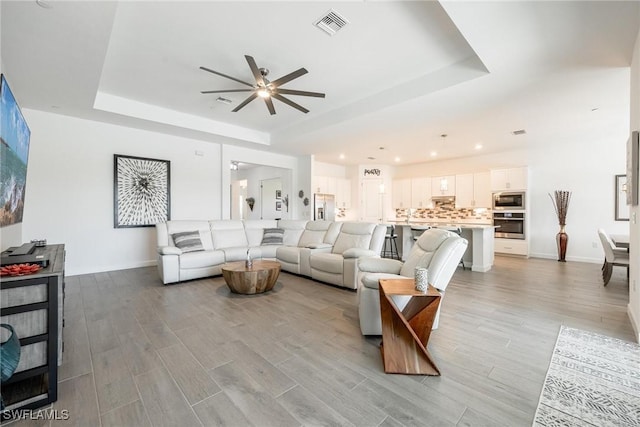 living room featuring ceiling fan and a raised ceiling