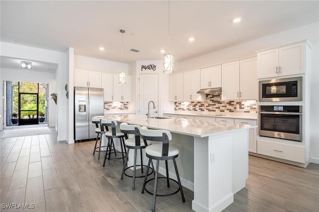 kitchen featuring stainless steel appliances, a sink, white cabinetry, light countertops, and an island with sink