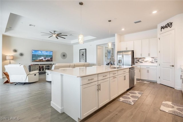 kitchen with stainless steel appliances, white cabinets, open floor plan, light countertops, and a center island with sink