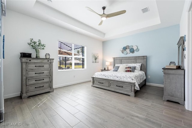 bedroom featuring a ceiling fan, baseboards, visible vents, light wood-style floors, and a tray ceiling