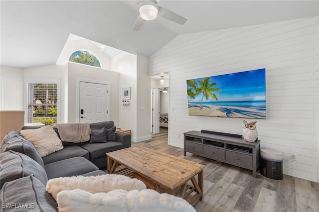 living room featuring ceiling fan, high vaulted ceiling, light wood-type flooring, and wooden walls