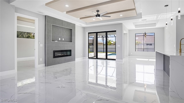 unfurnished living room featuring a tray ceiling, ceiling fan, and a tiled fireplace