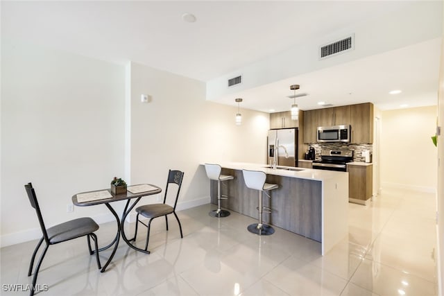 kitchen with sink, appliances with stainless steel finishes, light tile patterned floors, backsplash, and decorative light fixtures