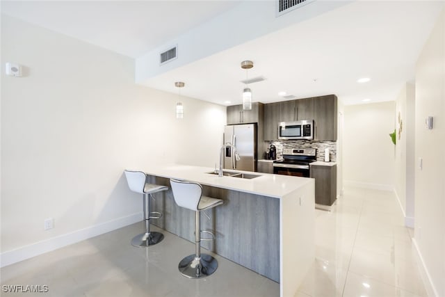 kitchen featuring dark brown cabinetry, light tile patterned flooring, appliances with stainless steel finishes, decorative light fixtures, and decorative backsplash