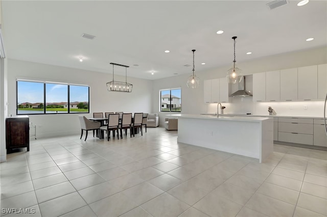 kitchen with hanging light fixtures, sink, a kitchen island with sink, and wall chimney range hood