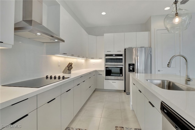 kitchen with wall chimney range hood, stainless steel appliances, sink, light tile patterned floors, and white cabinets