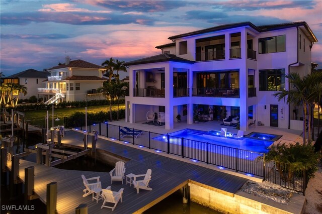 pool at dusk with an in ground hot tub, a boat dock, and a patio area