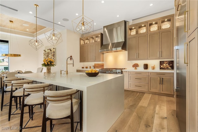 kitchen featuring pendant lighting, sink, a large island, wall chimney exhaust hood, and light hardwood / wood-style flooring