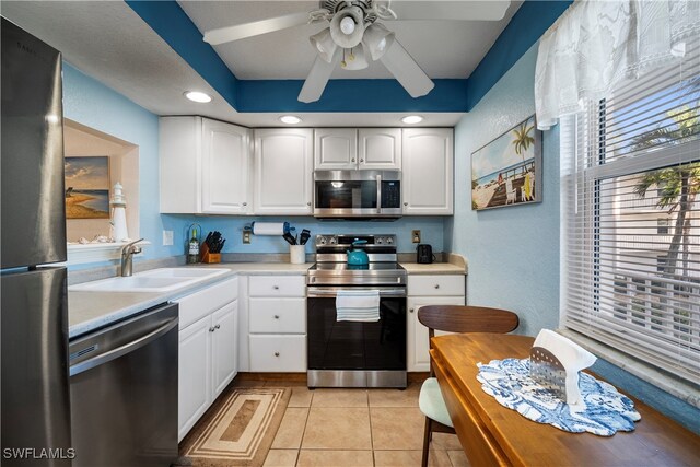 kitchen with appliances with stainless steel finishes, light tile patterned flooring, sink, white cabinetry, and ceiling fan