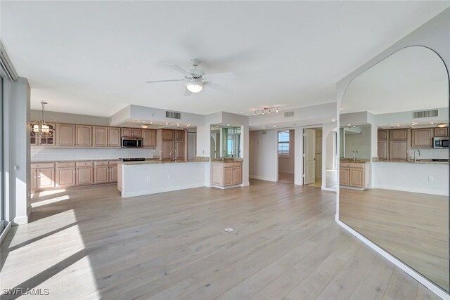 kitchen with ceiling fan with notable chandelier, decorative backsplash, sink, light wood-type flooring, and decorative light fixtures