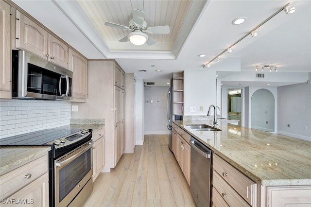 kitchen featuring sink, appliances with stainless steel finishes, light brown cabinetry, a tray ceiling, and light wood-type flooring