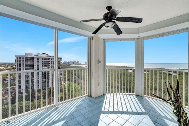 unfurnished sunroom featuring ceiling fan, a view of the beach, and a water view