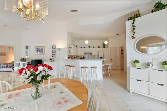 tiled dining area featuring a high ceiling and ceiling fan with notable chandelier