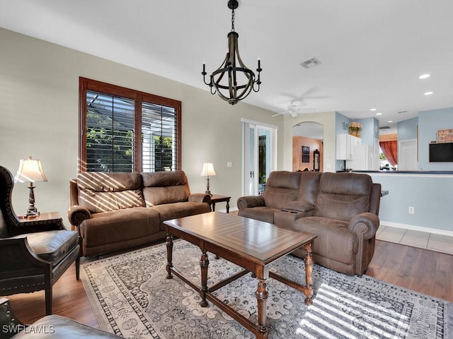 living room featuring ceiling fan with notable chandelier and light hardwood / wood-style flooring