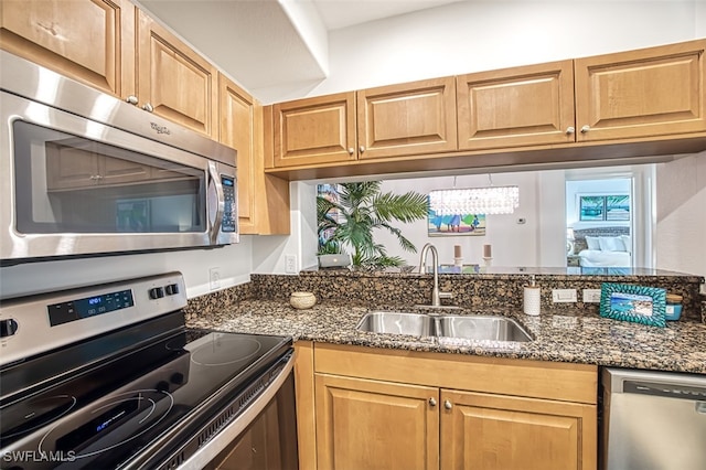 kitchen featuring an inviting chandelier, stainless steel appliances, sink, and dark stone counters