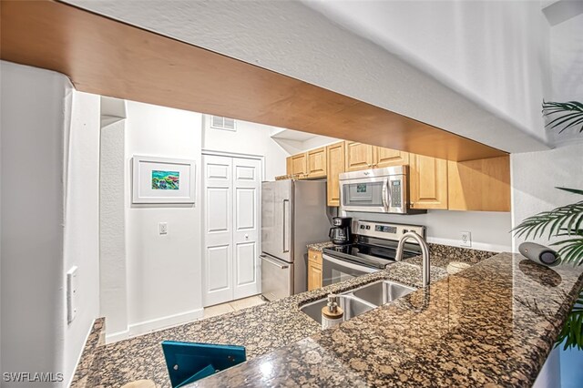 kitchen featuring appliances with stainless steel finishes, kitchen peninsula, dark stone counters, light tile patterned floors, and light brown cabinets