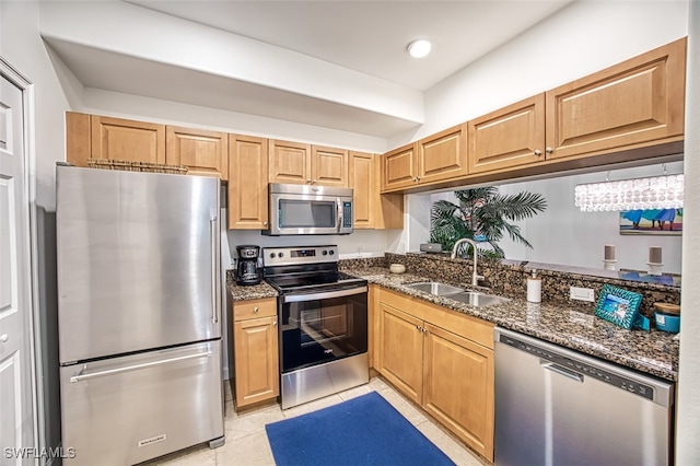 kitchen with stainless steel appliances, light tile patterned flooring, sink, and dark stone countertops