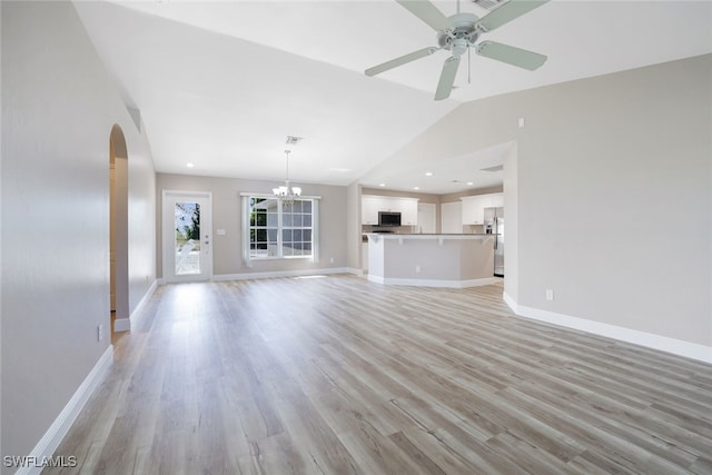 unfurnished living room with ceiling fan with notable chandelier, vaulted ceiling, and light hardwood / wood-style flooring