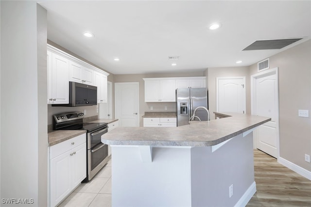 kitchen featuring white cabinetry, a kitchen breakfast bar, an island with sink, light hardwood / wood-style floors, and appliances with stainless steel finishes