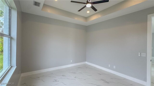 spare room with a tray ceiling, plenty of natural light, and ceiling fan