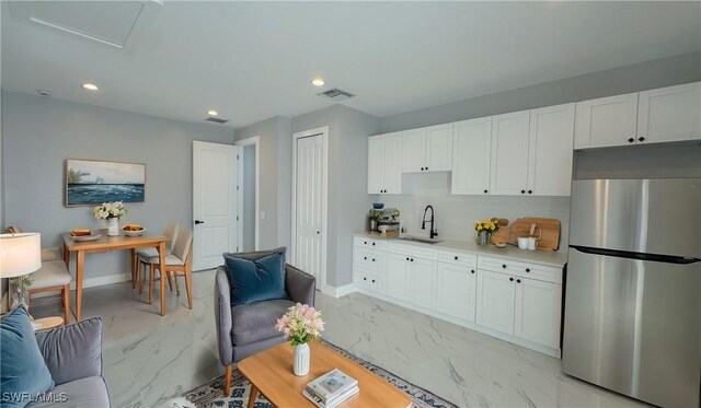 kitchen with white cabinetry, sink, and stainless steel fridge