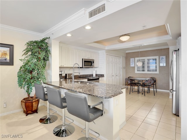 kitchen with stainless steel appliances, dark stone counters, a breakfast bar, white cabinets, and kitchen peninsula