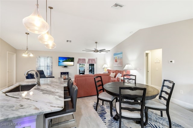 dining room with ceiling fan with notable chandelier, light hardwood / wood-style flooring, sink, and vaulted ceiling