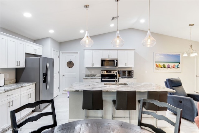 kitchen with stainless steel appliances, white cabinetry, decorative light fixtures, lofted ceiling, and a kitchen island with sink