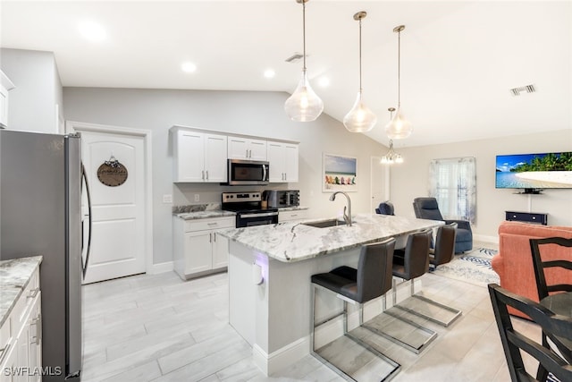 kitchen with white cabinets, a kitchen island with sink, light stone countertops, pendant lighting, and appliances with stainless steel finishes