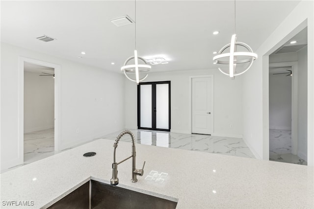 kitchen featuring light stone countertops, sink, hanging light fixtures, and ceiling fan with notable chandelier