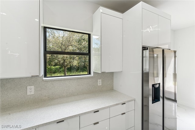 kitchen with stainless steel refrigerator with ice dispenser, white cabinetry, tasteful backsplash, and light stone countertops