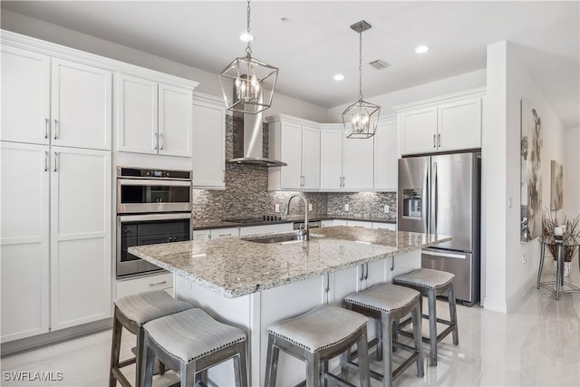 kitchen with a kitchen island with sink, wall chimney range hood, sink, appliances with stainless steel finishes, and white cabinetry