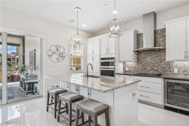 kitchen featuring white cabinets, wall chimney range hood, hanging light fixtures, sink, and wine cooler