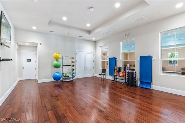 workout area with a tray ceiling and dark wood-type flooring