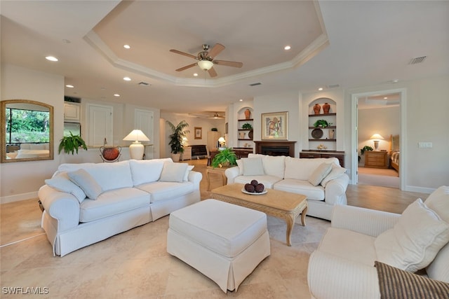 living room featuring crown molding, ceiling fan, built in shelves, and a raised ceiling