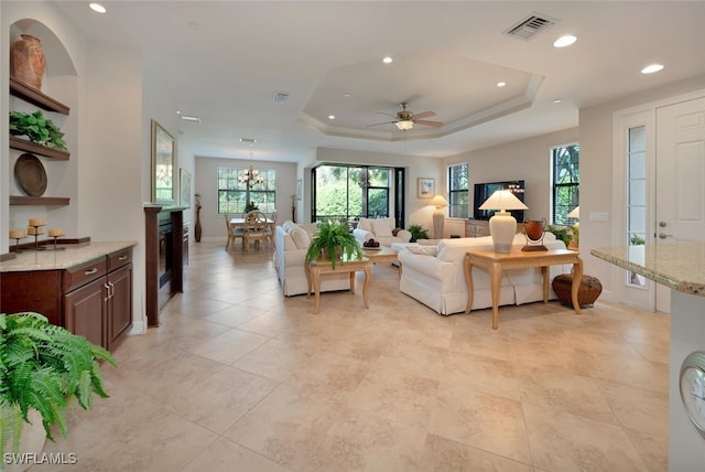 living room with a tray ceiling and ceiling fan with notable chandelier