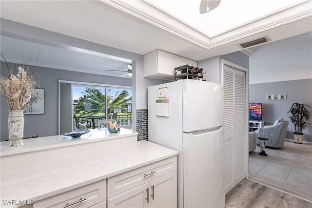 kitchen featuring white cabinetry, light hardwood / wood-style floors, ceiling fan, light stone counters, and white refrigerator