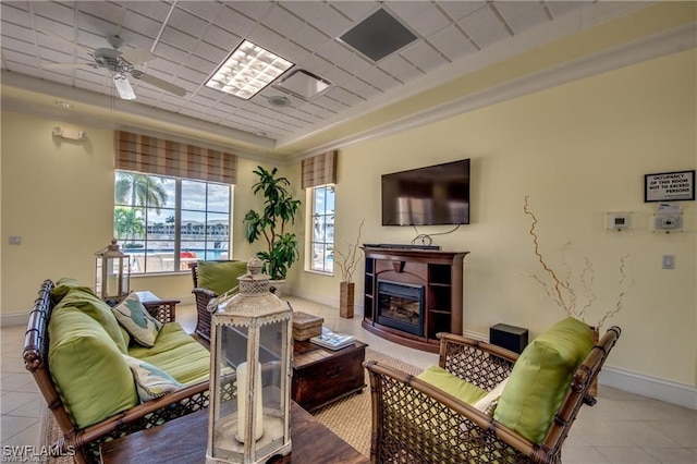 living room with ceiling fan, a tray ceiling, ornamental molding, and light tile patterned floors