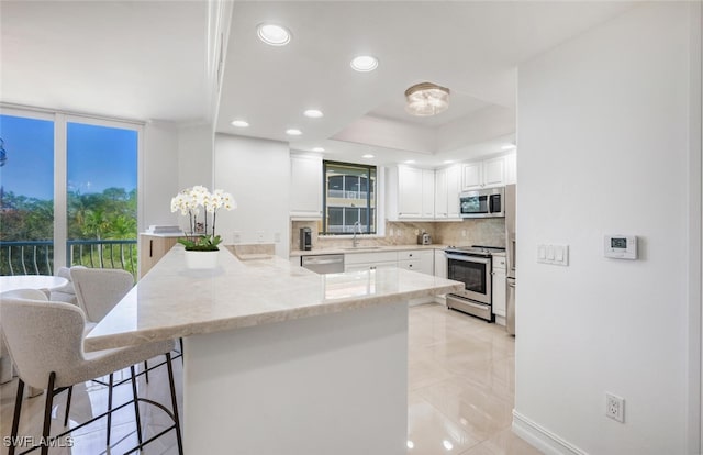 kitchen featuring a sink, white cabinetry, stainless steel appliances, a peninsula, and decorative backsplash