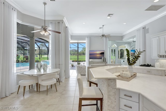 kitchen featuring white cabinetry, light tile patterned flooring, a kitchen bar, ornamental molding, and ceiling fan