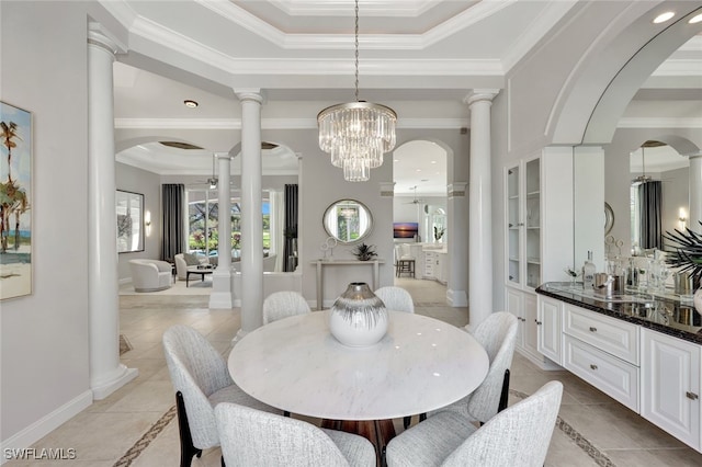 tiled dining area with crown molding, a raised ceiling, a chandelier, and decorative columns