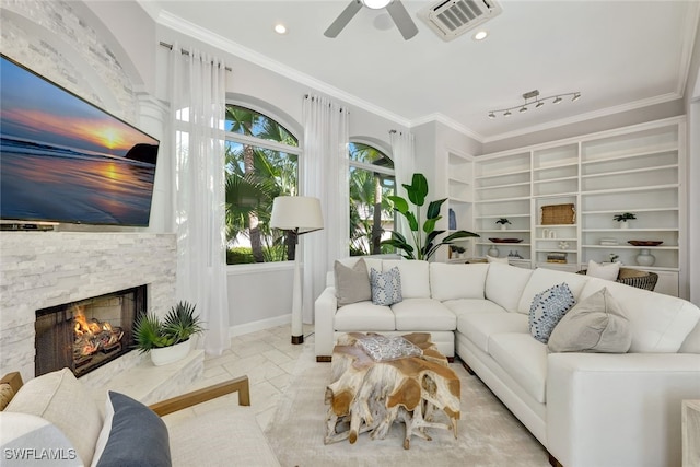 living room with built in shelves, ceiling fan, ornamental molding, and a stone fireplace