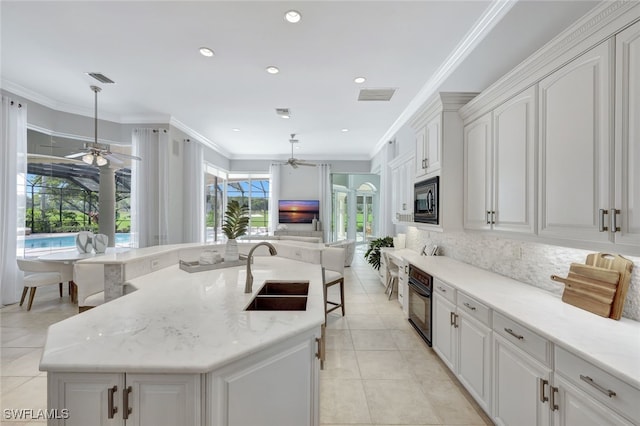 kitchen with white cabinets, an island with sink, built in microwave, pendant lighting, and sink